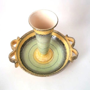 以下が含まれることがあります： 黄色、緑、黒の釉薬をかけたセラミック製のサービングディッシュ。ディッシュにはハンドルが2つと、中央にマッチする釉薬をかけた台座があります。