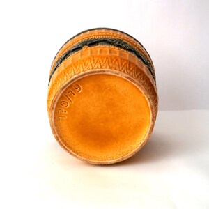 May include: A cylindrical ceramic vessel with a glossy orange base and a dark green upper section featuring embossed geometric patterns. The bottom of the piece is stamped with the text 170/19, indicating a specific model number.