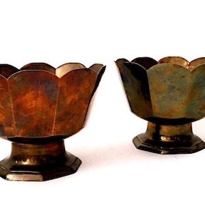 May include: Two antique metal bowls with a scalloped rim and pedestal base. The bowls have a bronze finish with variations in colour, ranging from brown to green. The bowls are likely decorative or for serving.