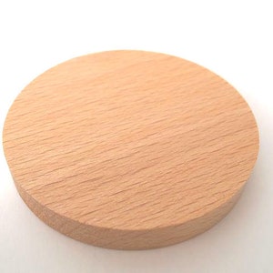 May include: A round, light brown wooden coaster. The coaster is smooth and has a natural wood grain.
