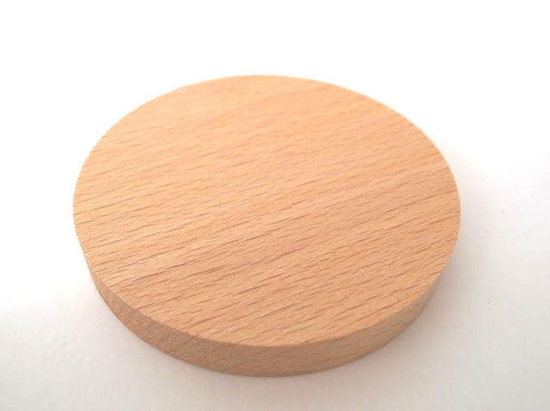 May include: A round, light brown wooden coaster. The coaster is smooth and has a natural wood grain.