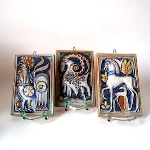 May include: Three ceramic wall plaques with raised relief designs of a rooster, a goat, and a horse. The plaques are painted in shades of blue, brown, white, and yellow.