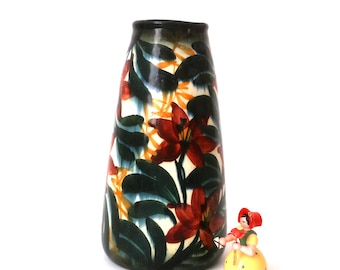 May include: A tall, ceramic vase with a conical shape. The vase is decorated with a floral pattern of red, orange, and yellow flowers with green leaves on a white background. The vase has a dark green glaze.