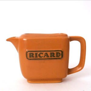 Könnte beinhalten: Ein kleiner, orangefarbener Keramik-Milchkännchen mit Henkel und der Aufschrift "RICARD" in goldenen Buchstaben.