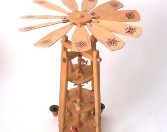 May include: A tiered wooden Christmas pyramid featuring a rotating top fan with star patterns. The structure has three levels holding small carved figures, including a deer and a red-clad character. Four metal candle holders are at the base.