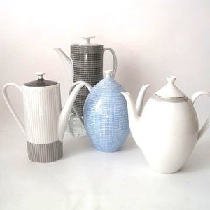 May include: Four ceramic teapots in different colours and patterns. The teapots are white, brown, blue, and white with a brown stripe. They are all on a white background.