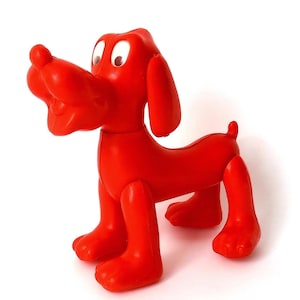 May include: A bright red plastic dog toy with white eyes. The dog has a long snout, floppy ears, and a small tail. The toy is standing on all fours, with its legs slightly bent. The toy is a solid color and appears to be made of plastic.