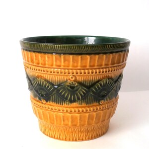 May include: A ceramic plant pot featuring a vibrant mustard yellow glaze with a contrasting dark forest green band around the rim and a central horizontal relief pattern of repeating fan-shaped motifs and small circular accents.