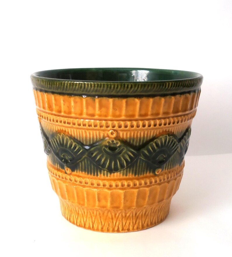 May include: A ceramic plant pot featuring a vibrant mustard yellow glaze with a contrasting dark forest green band around the rim and a central horizontal relief pattern of repeating fan-shaped motifs and small circular accents.