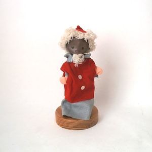 May include: A vintage hand puppet with a brown face, white beard, and red and white clothing. The puppet is standing on a wooden base.