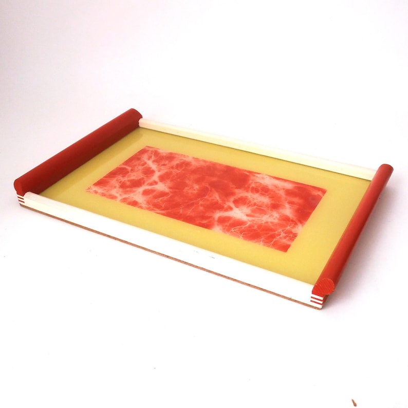 May include: A rectangular tray with a yellow base and red edges. The tray has a red marbled design in the center.