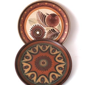 May include: Two decorative ceramic plates. The top plate features a brown owl perched on a branch with floral accents. The bottom plate has a symmetrical design in shades of brown, orange, and green. Both plates have a brown border.