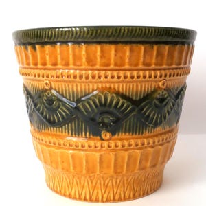 May include: A ceramic planter featuring a vibrant mustard yellow glaze with a dark forest green rim and a central band of embossed fan-shaped patterns. The exterior surface is textured with vertical ridges and geometric detailing.