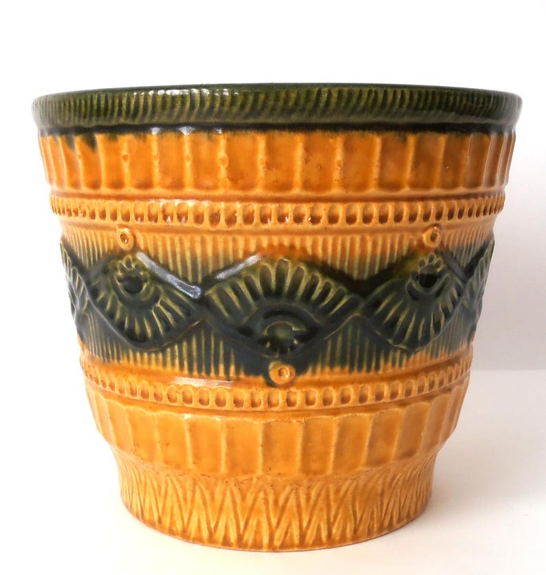 May include: A ceramic planter featuring a vibrant mustard yellow glaze with a dark forest green rim and a central band of embossed fan-shaped patterns. The exterior surface is textured with vertical ridges and geometric detailing.