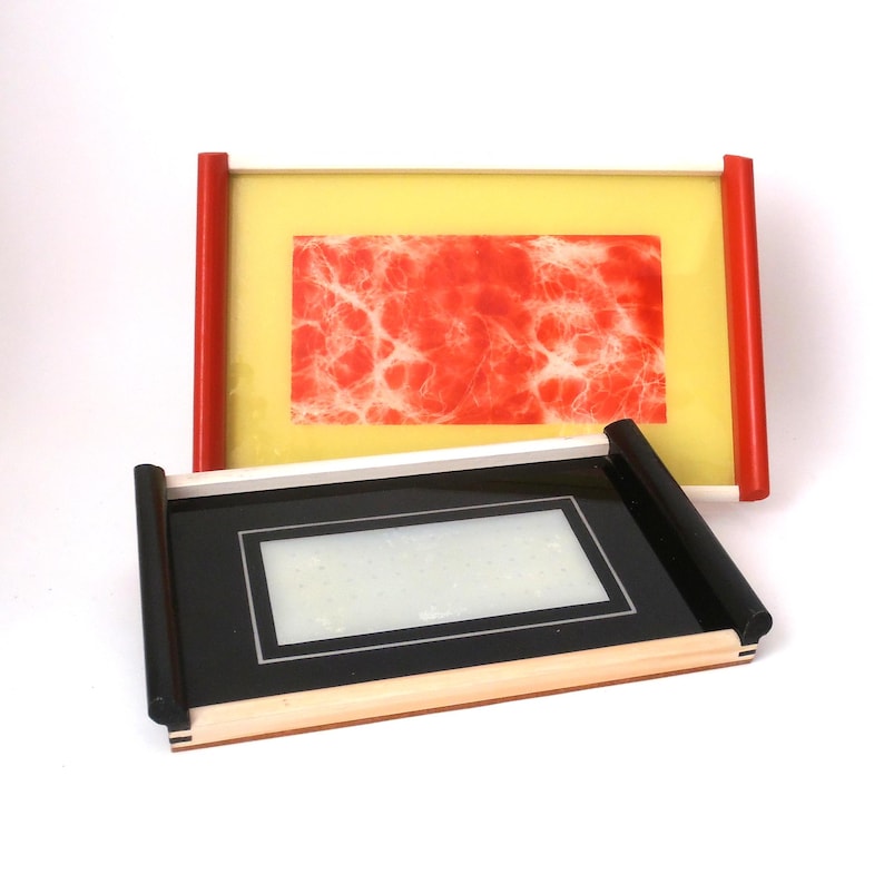 May include: Two decorative trays, one with a yellow base and red marbled design, and the other with a black base and a wood frame.