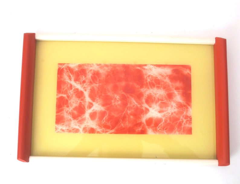 May include: A red and white tray with a white frame and a red border. The tray has a yellow background and a red and white abstract design in the center.