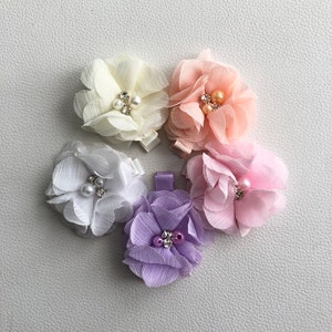 May include: Five flower hair clips with pearl and rhinestone embellishments. The clips are in shades of white, pink, and purple.
