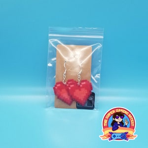 May include: A pair of red pixel heart earrings on a brown card with a white background. The earrings are hanging from silver hooks.