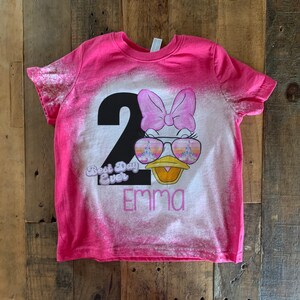 May include: Pink bleached t-shirt with a black number 2, a cartoon duck wearing sunglasses, a pink bow, and the text "Best Day Ever" and "Emma".