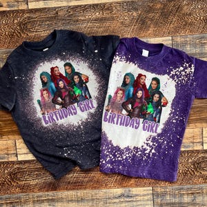 May include: Two purple and black t-shirts with a bleach splattered design. The shirts feature a group of cartoon characters with the text "Birthday Girl" on each shirt.