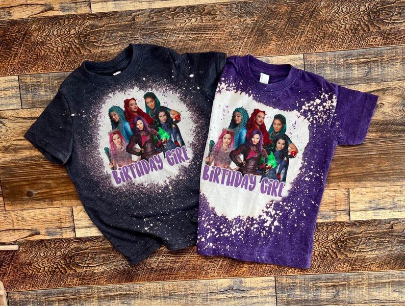 May include: Two purple and black t-shirts with a bleach splattered design. The shirts feature a group of cartoon characters with the text "Birthday Girl" on each shirt.