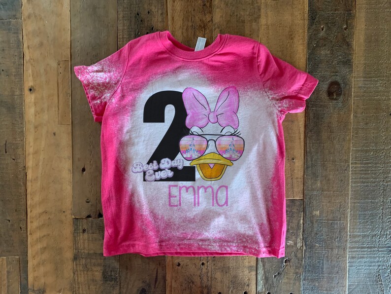May include: Pink bleached t-shirt with a black number 2, a cartoon duck wearing sunglasses, a pink bow, and the text "Best Day Ever" and "Emma".