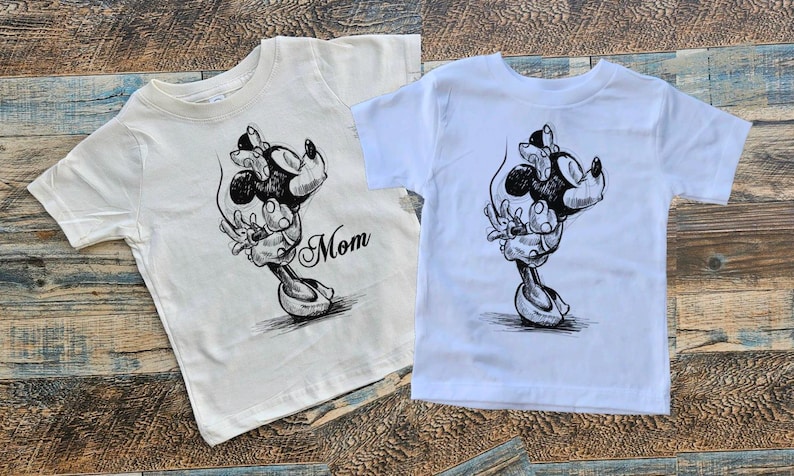 May include: Two white t-shirts with a black and white illustration of Mickey Mouse and Minnie Mouse. The shirt on the left says "Mom" on the bottom right corner.
