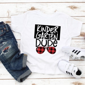 May include: White t-shirt with black text that says "Kinder Garden Dude" and red and black plaid sunglasses.