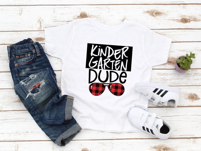May include: White t-shirt with black text that says "Kinder Garden Dude" and red and black plaid sunglasses.