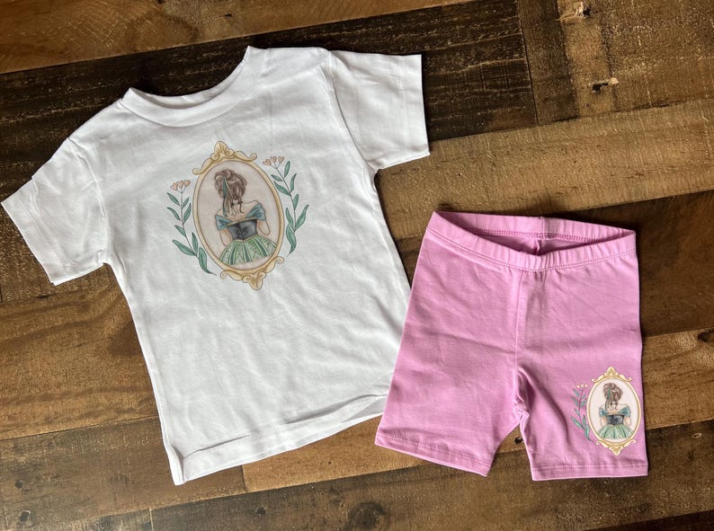 Peut inclure: Un t-shirt blanc avec un motif floral et une fille en robe verte dans un cadre. Un short rose avec un motif floral similaire et une fille en robe verte dans un cadre.