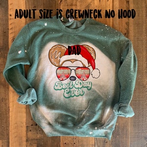 May include: Green sweatshirt with a bleached effect featuring a cartoon Mickey Mouse head with a Santa hat and sunglasses. The sunglasses reflect the Cinderella Castle. The text "Dad" is on the hat and "Best Day Ever" is below the sunglasses.