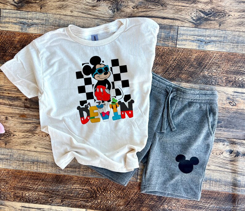May include: White t-shirt with a black and white checkered background, a cartoon Mickey Mouse wearing sunglasses, and the name "DEVIN" in colorful letters. Gray sweatpants with a black Mickey Mouse silhouette.