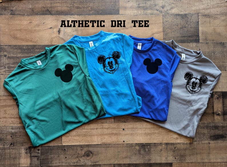May include: Four athletic dri-fit tees in teal, light blue, royal blue, and gray. Each shirt features a black Mickey Mouse graphic. The shirts are displayed on a wooden surface. The text "ALTHETIC DRI TEE" is at the top.