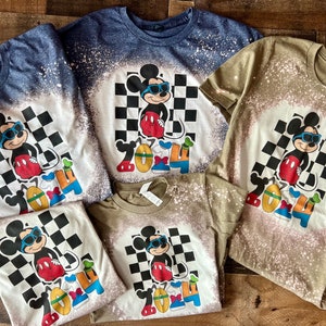 May include: Four bleached t-shirts with a cartoon image of Mickey Mouse wearing sunglasses and standing in front of a checkered pattern. The text "2024" is below Mickey Mouse. The shirts are in different colors: blue, green, white, and white.