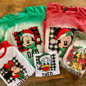 May include: Five green, red, and white t-shirts with a bleach-splattered effect. Each shirt features a different Disney character wearing a Santa hat and a plaid scarf. The shirts are labeled "Dad", "Everly", "Theo", "Theodore", and "Mom".