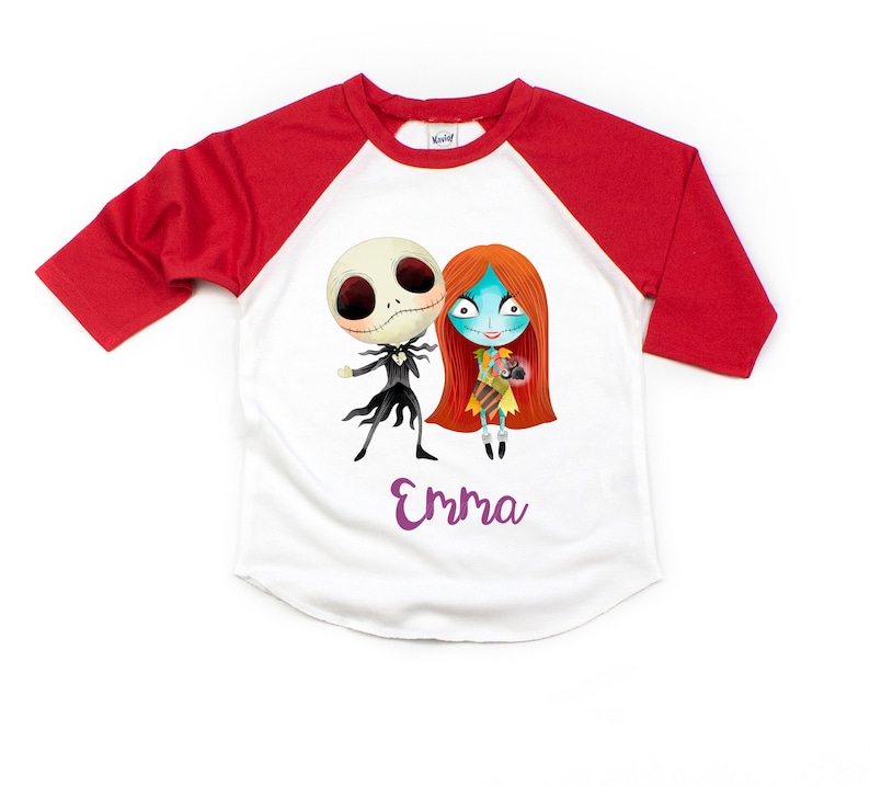 Puede incluir: Camiseta de b&eacute;isbol blanca y roja con una imagen de dibujos animados de Jack Skellington y Sally de Pesadilla antes de Navidad. La camiseta tiene el nombre "Emma" impreso en morado debajo de la imagen.