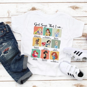 May include: White t-shirt with a graphic of Disney princesses and bible verses. The text reads "God Says That I am..."  The shirt is paired with blue jeans and white sneakers with black stripes.