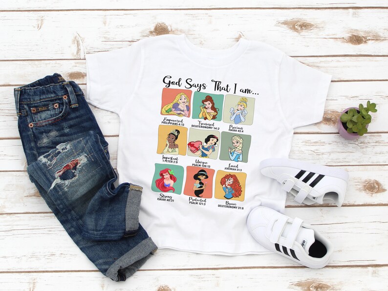 May include: White t-shirt with a graphic of Disney princesses and bible verses. The text reads "God Says That I am..."  The shirt is paired with blue jeans and white sneakers with black stripes.
