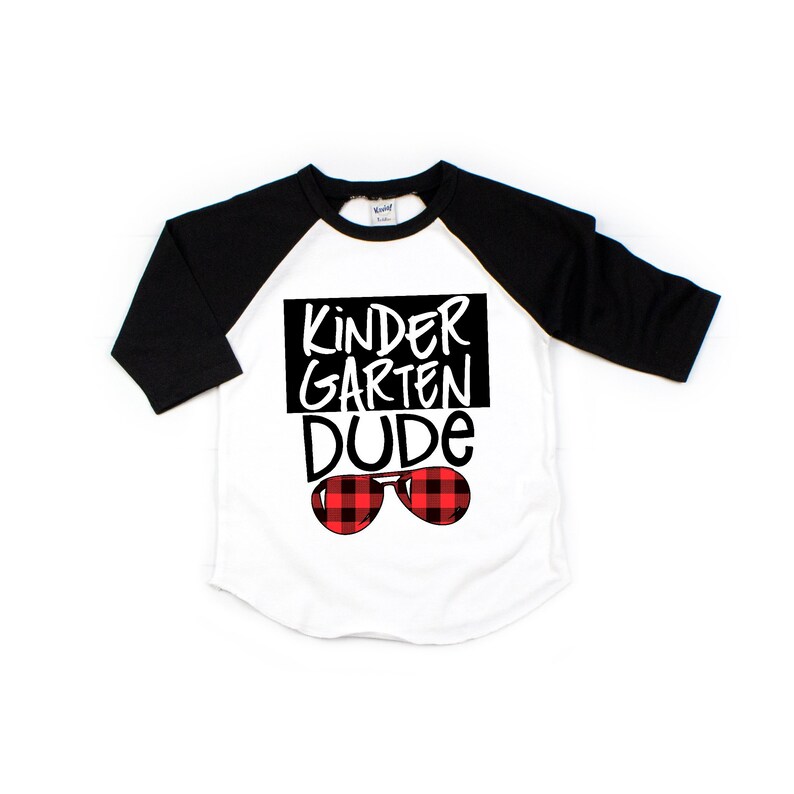 May include: White and black baseball tee shirt with red and black plaid sunglasses and the text "Kindergarten Dude" in black.