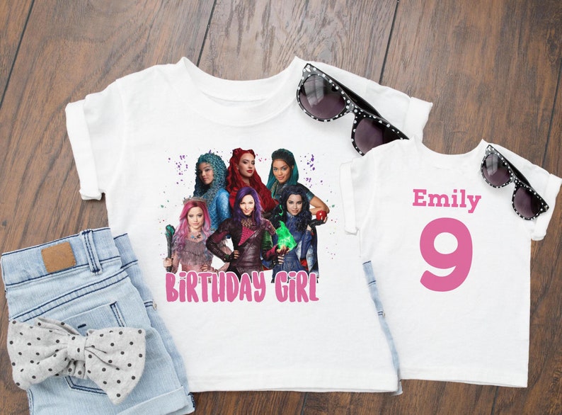 May include: Two white t-shirts with a graphic of the Disney Descendants characters. The larger shirt says "Birthday Girl" in pink letters. The smaller shirt has the name "Emily" and the number "9" in pink letters.