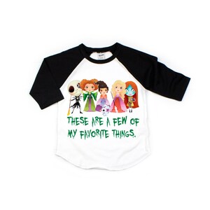Puede incluir: Una camiseta de b&eacute;isbol blanca y negra con un gr&aacute;fico verde de personajes de pel&iacute;culas populares de Halloween. El texto "These are a few of my favorite things." est&aacute; impreso en verde debajo del gr&aacute;fico.