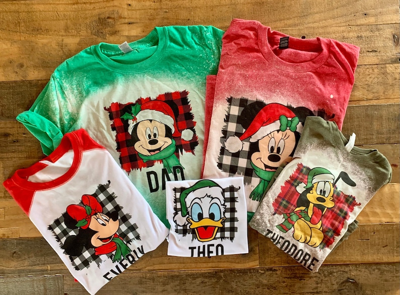 May include: Five Christmas-themed t-shirts with bleach-splattered designs featuring Mickey Mouse, Minnie Mouse, and Donald Duck characters. The shirts have the names "Dad", "Everly", "Theo", and "Theodore" printed on them.