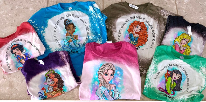 Peut inclure: Une collection de huit t-shirts blanchis et tie-dye repr&eacute;sentant des princesses Disney. Chaque t-shirt pr&eacute;sente une princesse diff&eacute;rente et une citation du film. Les t-shirts sont de diff&eacute;rentes couleurs, notamment bleu, vert, rose, violet et rouge.