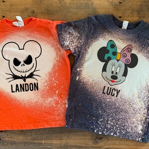 Puede incluir: Dos camisetas blanqueadas con tem&aacute;tica de Halloween. Una camiseta naranja presenta un dise&ntilde;o de Jack Skellington en blanco y negro con el nombre Landon. La otra camiseta azul presenta un dise&ntilde;o de Minnie Mouse con el nombre Lucy.