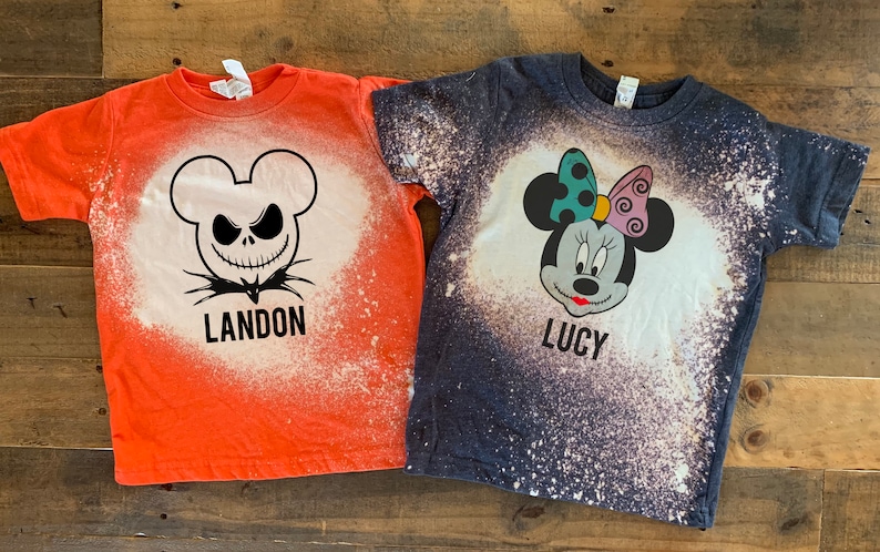 Puede incluir: Dos camisetas blanqueadas con tem&aacute;tica de Halloween. Una camiseta naranja presenta un dise&ntilde;o de Jack Skellington en blanco y negro con el nombre Landon. La otra camiseta azul presenta un dise&ntilde;o de Minnie Mouse con el nombre Lucy.