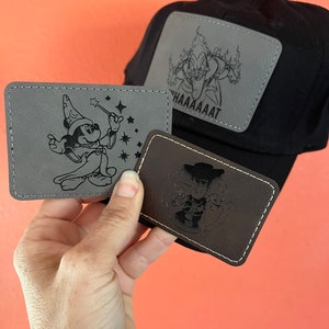 May include: Three embroidered patches featuring Disney characters. The first patch is gray and features Mickey Mouse dressed as a sorcerer. The second patch is brown and features Woody from Toy Story. The third patch is gray and features a character from the movie Fantasia. The patches are all stitched with a black thread.