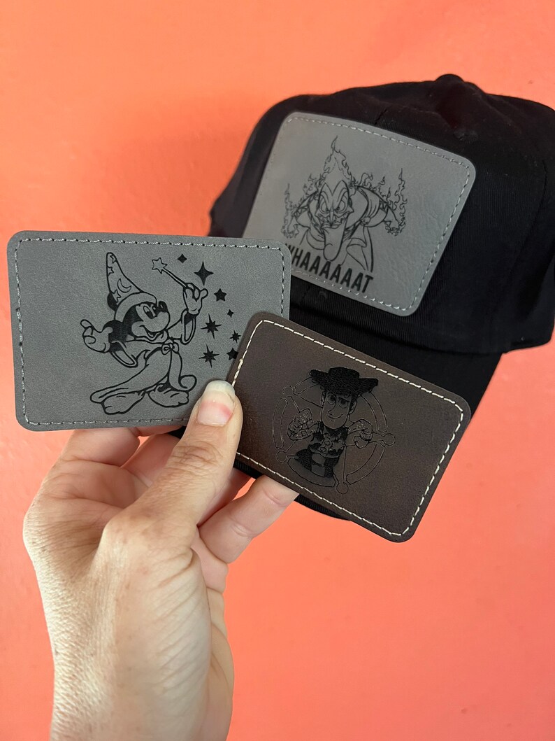 May include: Three embroidered patches featuring Disney characters. The first patch is gray and features Mickey Mouse dressed as a sorcerer. The second patch is brown and features Woody from Toy Story. The third patch is gray and features a character from the movie Fantasia. The patches are all stitched with a black thread.