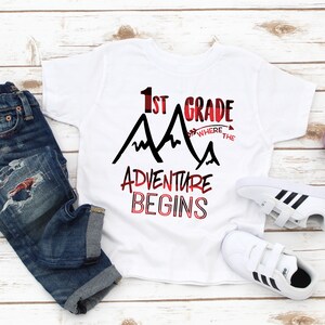 May include: White t-shirt with black text that reads "1st Grade Where the Adventure Begins" with a red and black mountain graphic.