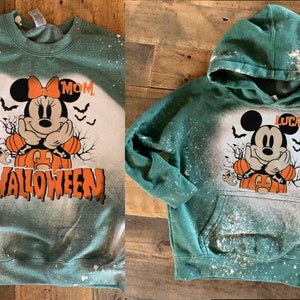 Puede incluir: Sudaderas verdes con un dise&ntilde;o salpicado de lej&iacute;a que presenta una imagen de dibujos animados de Mickey Mouse vestido de calabaza. Una sudadera dice "MOM" y la otra dice "LUCAS".