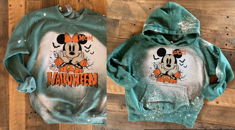 Puede incluir: Sudaderas verdes con un dise&ntilde;o salpicado de lej&iacute;a que presenta una imagen de dibujos animados de Mickey Mouse vestido de calabaza. Una sudadera dice "MOM" y la otra dice "LUCAS".